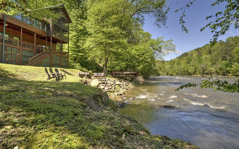 This gorgeous cabin has some of the most beautiful river frontage in all of Gilmer County. This section of the Coosawattee River cascades over rocks creating "water music" that will soothe your soul. The cabin has a very large great room that overlooks the river and features a dramatic stone fireplace, a large dining area, and a spacious kitchen with huge breakfast bar. Outside the great room, there is a wide covered deck and screened porch where you can enjoy the sights and sounds of the river. The lower level has a large game room, with a second fireplace, where you can gather for a game or watch TV. The upper level has a large loft as well has the master suite that also has a sunroom overlooking the river. The back yard has a concrete basketball court, fire pit area, and a dock on the river.